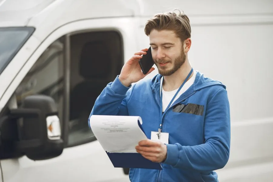 A local service technician answering a phone call next to a branded work van outside a customer's home