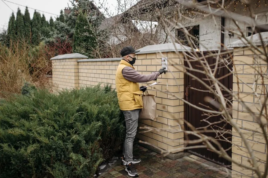 A uniformed home-services technician shaking hands with a homeowner on the front porch after a service call
