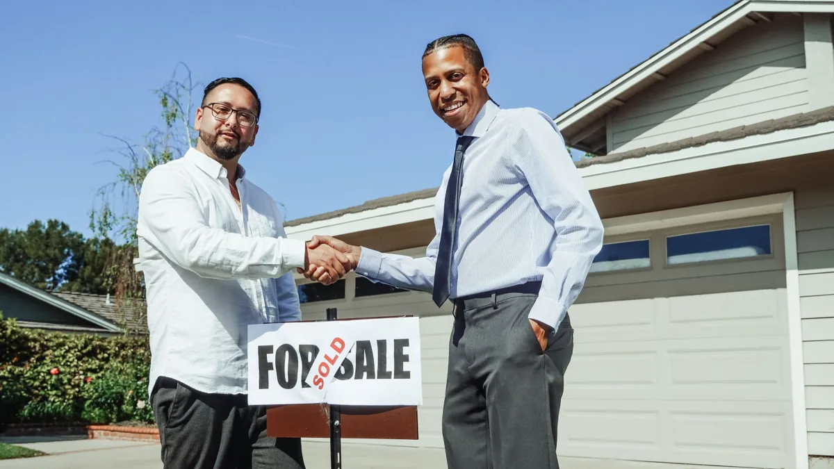 An HVAC technician shaking hands with a returning homeowner at the front door of a suburban house