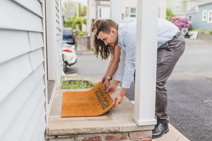 An HVAC technician shaking hands with a returning homeowner at the front door of a suburban house