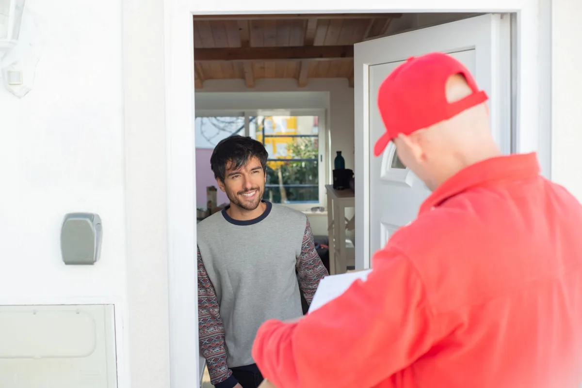 A uniformed home-service technician greeting a homeowner at the front door, tools in hand