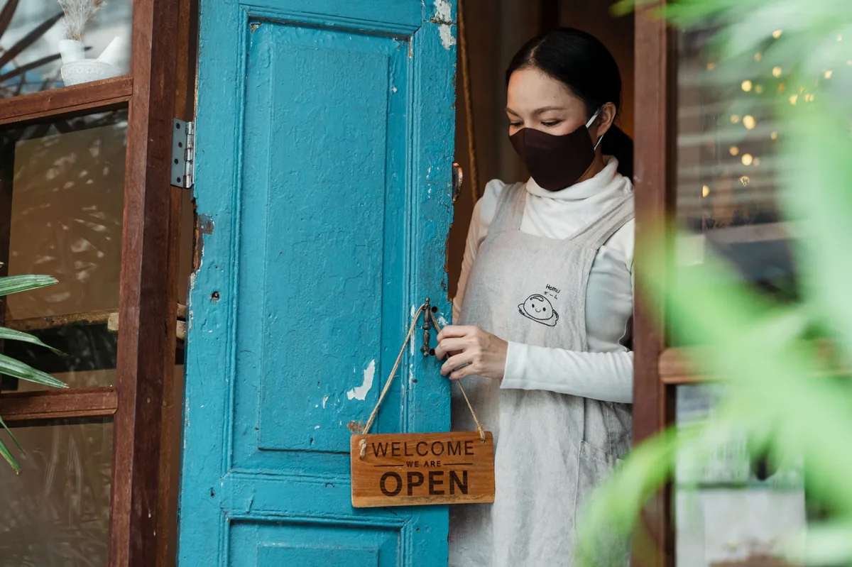 A local service business owner standing in the open doorway of their shopfront, shaking hands with an arriving customer