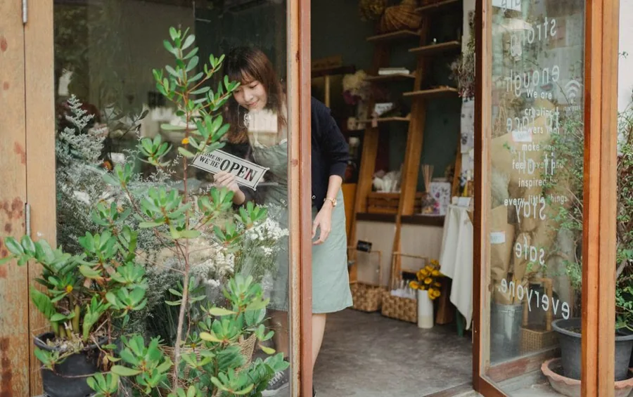 A local service business owner standing in the open doorway of their shopfront, shaking hands with an arriving customer