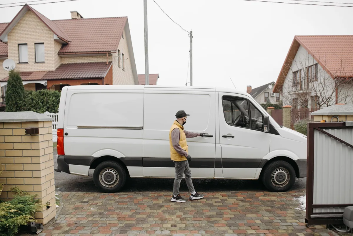 A uniformed service technician stepping out of a branded work van parked on a tree-lined residential street in a small town