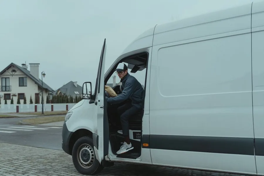 A uniformed service technician stepping out of a branded work van parked on a tree-lined residential street in a small town
