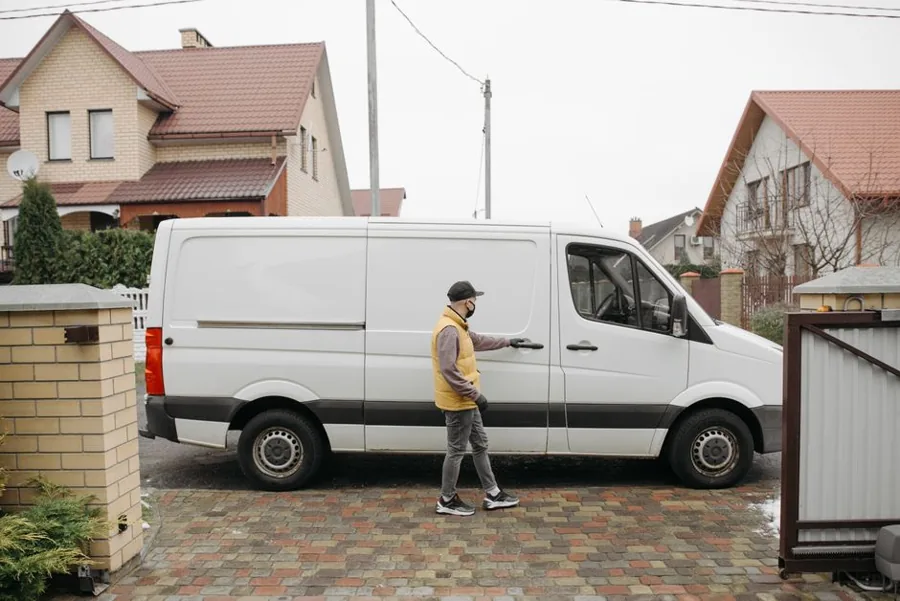 A uniformed service technician shaking hands with a homeowner at the front door of a house, with a branded work van parked at the curb.