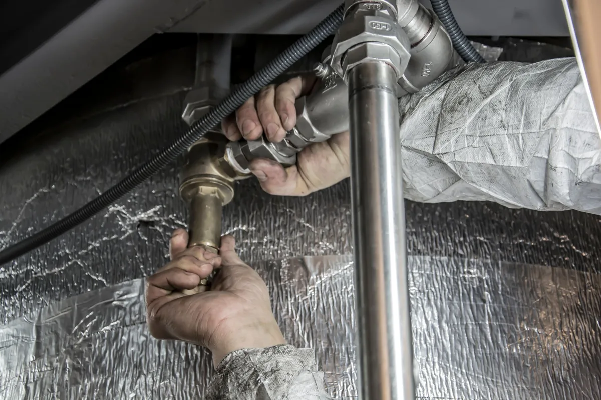 Plumber tightening a leaking pipe under a sink, a metaphor for fixing wasted ad spend