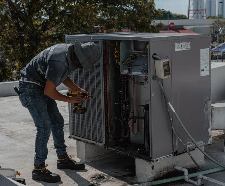 A service technician kneeling to repair outdoor equipment in a backyard, hands full, unable to reach a ringing phone